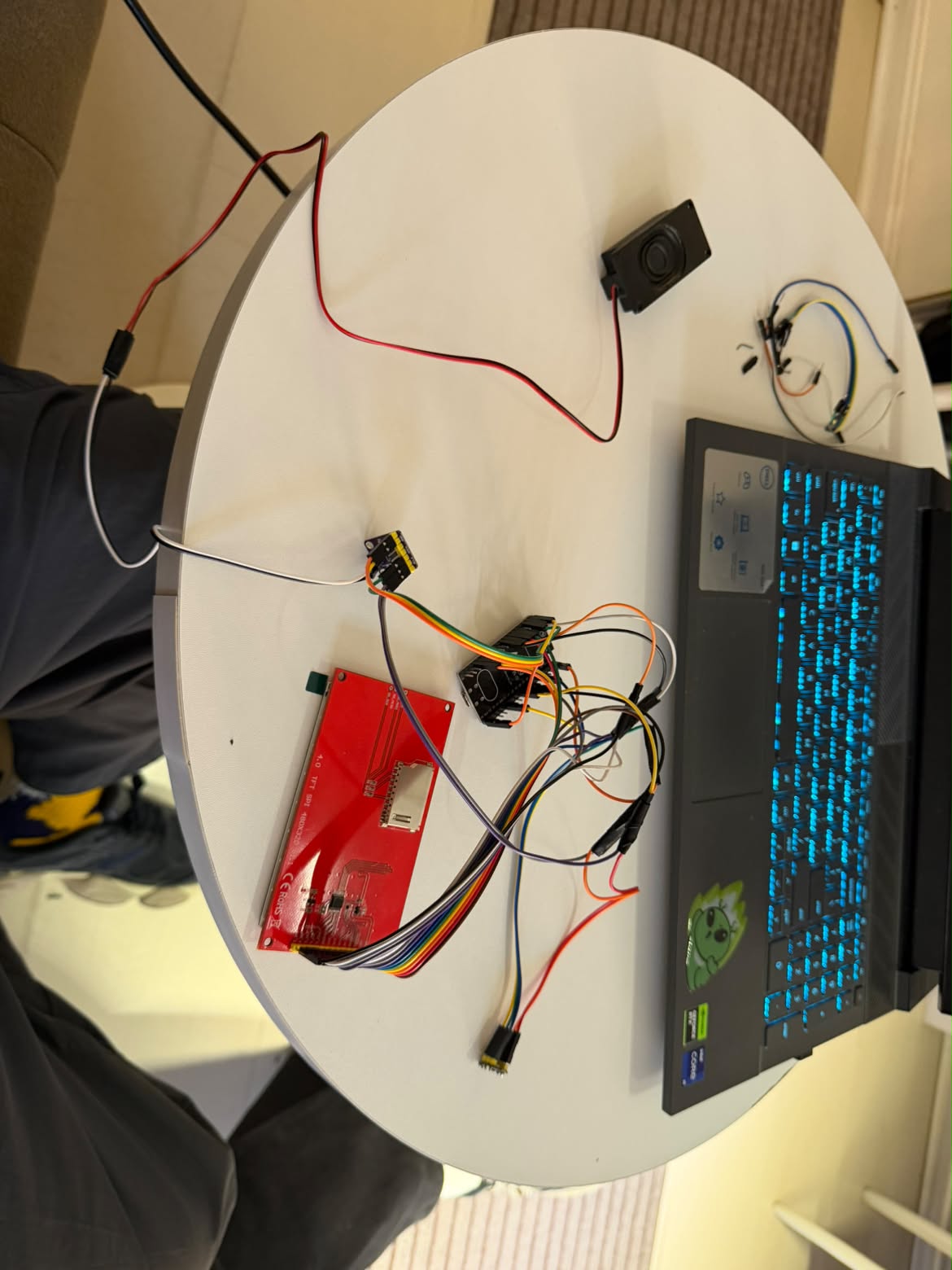 A red circuit board, wires and a laptop on a round table