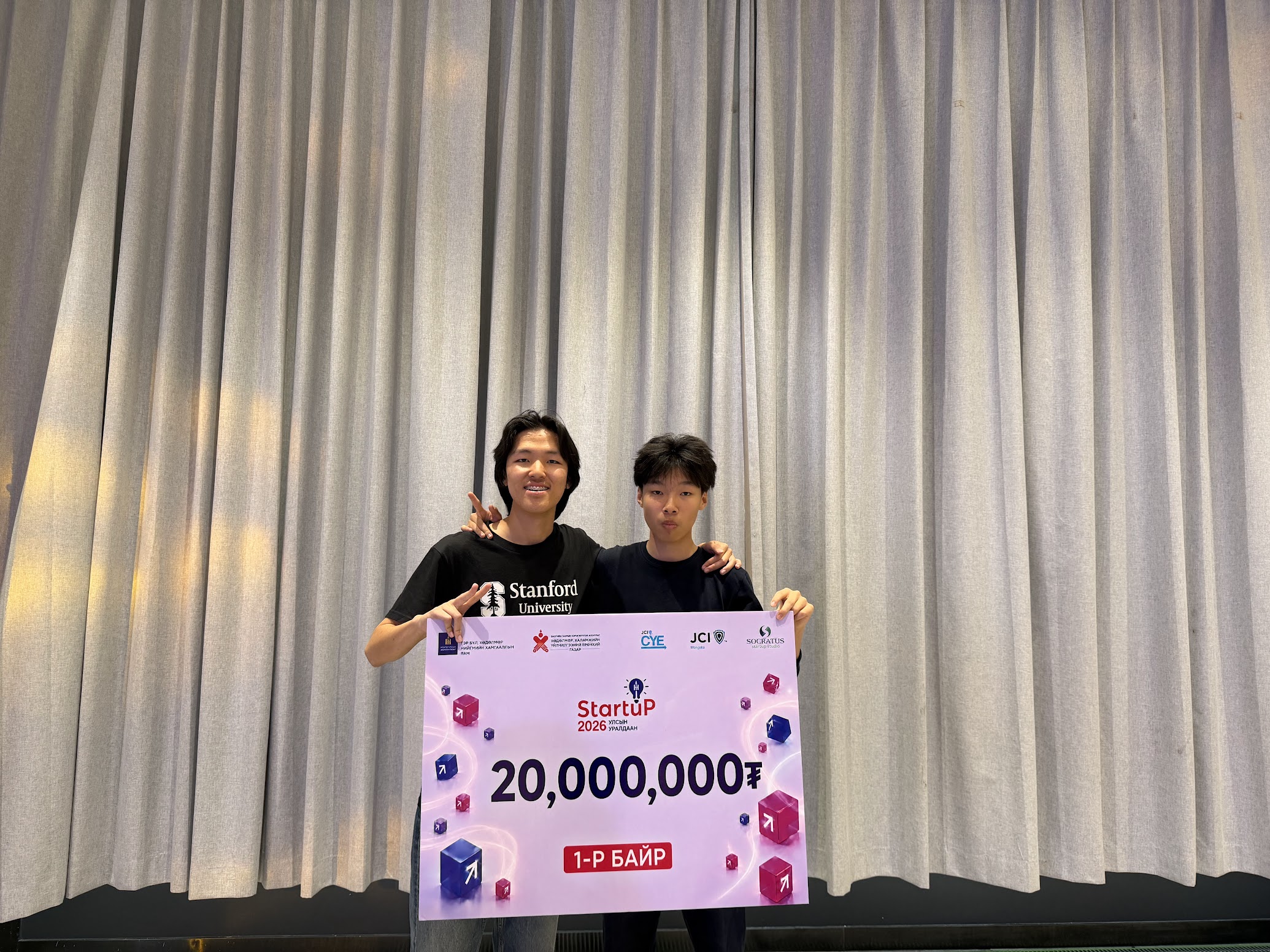 Itgel and a teammate on stage holding the first-place prize cheque